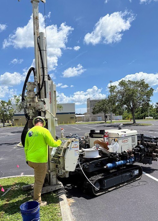 Field technician operating a track-mounted drilling rig beside a paved work area